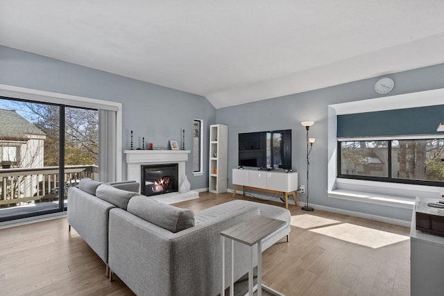 living area featuring vaulted ceiling, a glass covered fireplace, wood finished floors, and baseboards