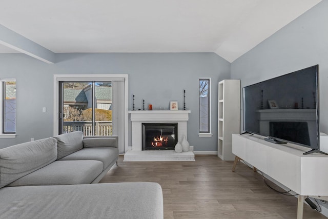 living area featuring a fireplace, baseboards, vaulted ceiling, and wood finished floors