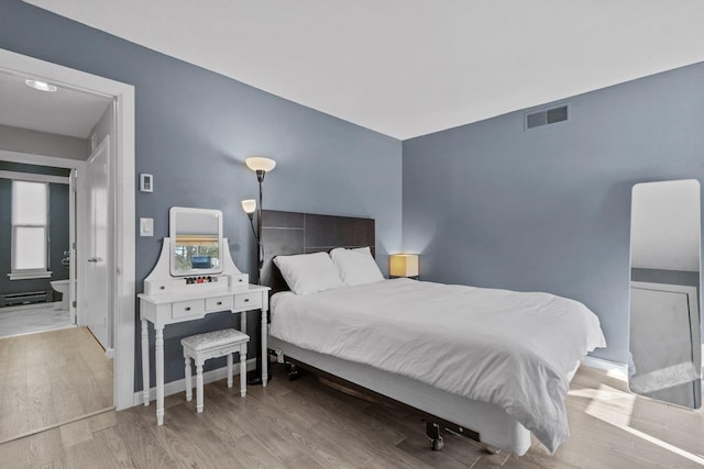 bedroom with a baseboard heating unit, visible vents, baseboards, and wood finished floors