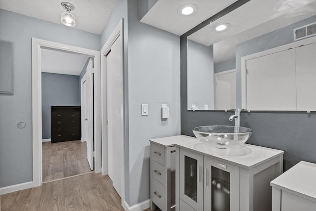 bathroom with visible vents, vanity, baseboards, and wood finished floors