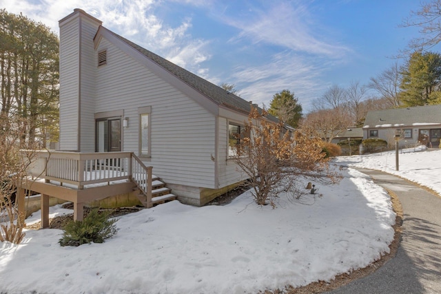 view of snow covered exterior with a chimney and a wooden deck