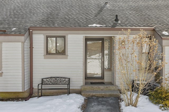 snow covered property entrance featuring a shingled roof