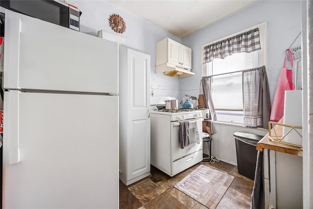 kitchen featuring under cabinet range hood, white cabinets, stone finish floor, and white appliances