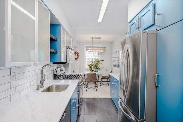 kitchen with appliances with stainless steel finishes, decorative light fixtures, tasteful backsplash, sink, and blue cabinetry