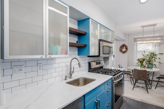 kitchen with appliances with stainless steel finishes, blue cabinets, sink, backsplash, and light stone countertops