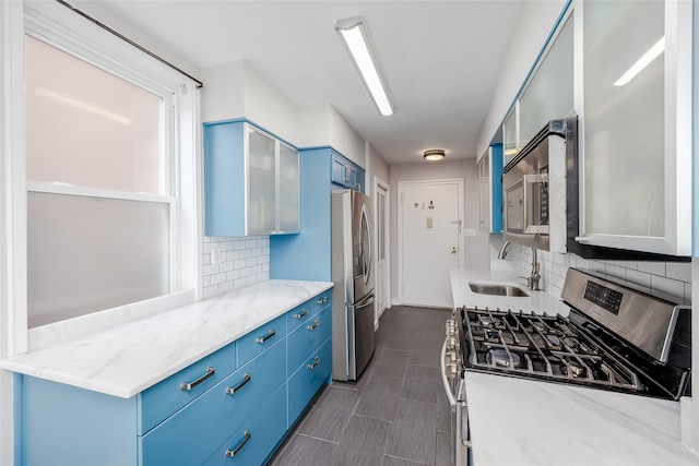 kitchen featuring sink, stainless steel appliances, tasteful backsplash, light stone countertops, and blue cabinets