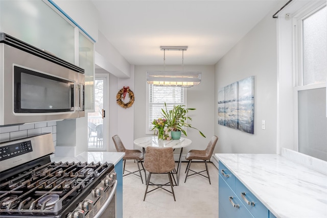 kitchen featuring blue cabinets, backsplash, hanging light fixtures, stainless steel appliances, and light stone countertops