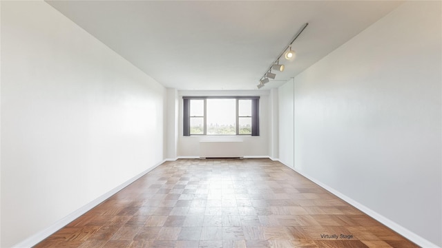 empty room with radiator heating unit, rail lighting, and baseboards