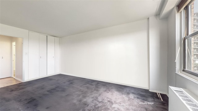 spare room featuring dark colored carpet, baseboards, and radiator heating unit