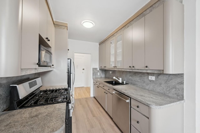 kitchen with light wood finished floors, tasteful backsplash, glass insert cabinets, stainless steel appliances, and a sink