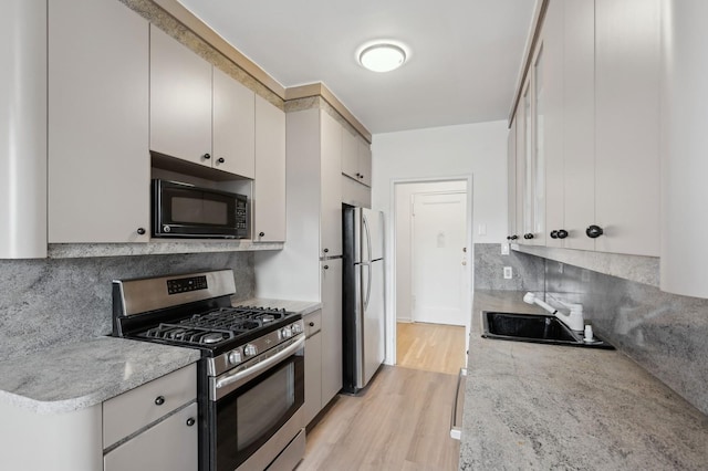 kitchen with light wood finished floors, appliances with stainless steel finishes, light stone counters, and a sink