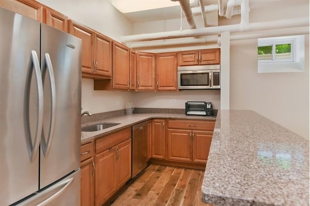 kitchen with brown cabinets, light stone countertops, stainless steel appliances, light wood-type flooring, and a sink