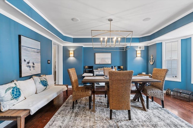 dining space featuring visible vents, a raised ceiling, ornamental molding, dark wood-style flooring, and a notable chandelier