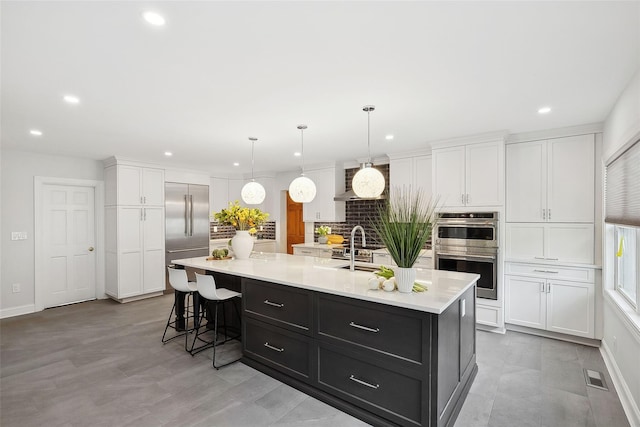 kitchen featuring pendant lighting, stainless steel appliances, light countertops, a kitchen island with sink, and white cabinetry