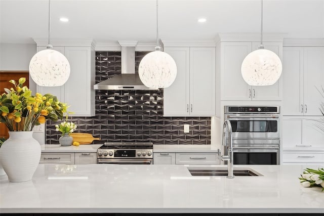 kitchen with white cabinets, wall chimney exhaust hood, appliances with stainless steel finishes, and light countertops