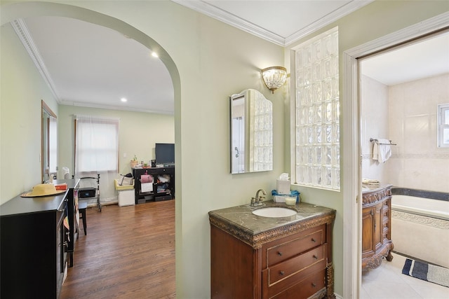 bathroom featuring wood finished floors, ornamental molding, a bathing tub, and vanity