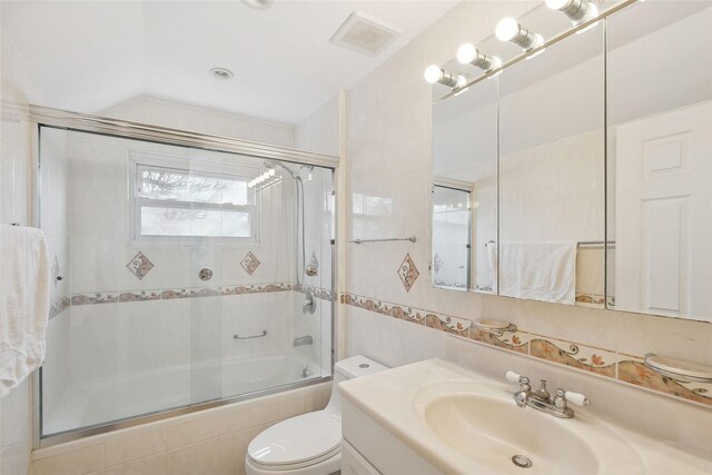 full bathroom with tile walls, visible vents, toilet, combined bath / shower with glass door, and vanity