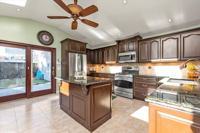 kitchen with dark brown cabinetry, a kitchen island, dark stone countertops, stainless steel appliances, and a sink