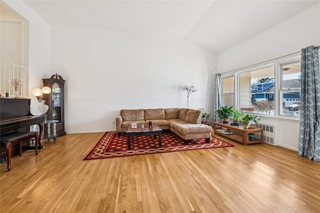 living area featuring radiator, light wood-type flooring, baseboards, and vaulted ceiling