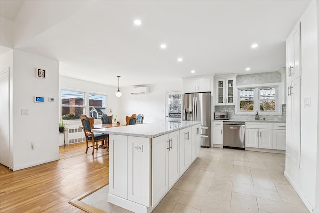 kitchen with stainless steel appliances, a sink, white cabinets, a wall mounted AC, and backsplash