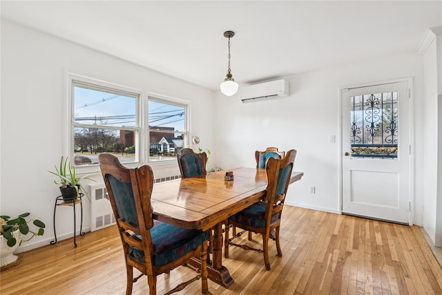 dining room with radiator, a wall unit AC, baseboards, and light wood finished floors