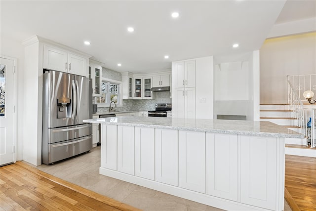 kitchen with stainless steel appliances, light wood-style flooring, decorative backsplash, a kitchen island, and under cabinet range hood