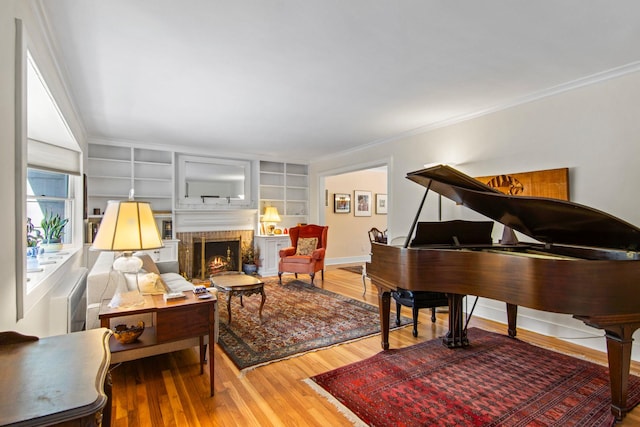 sitting room with a brick fireplace, crown molding, built in features, and hardwood / wood-style floors