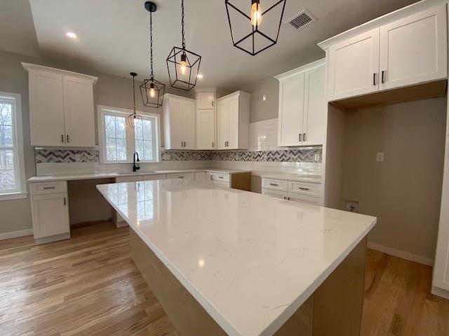 kitchen with white cabinetry, decorative light fixtures, sink, and a kitchen island