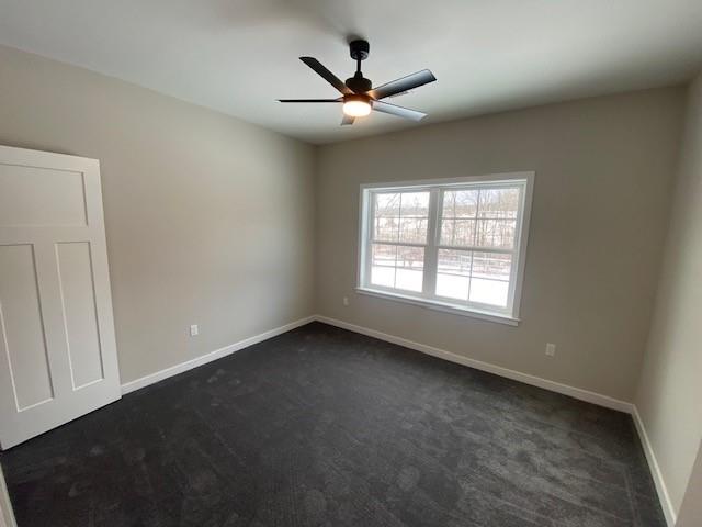 spare room featuring dark colored carpet and ceiling fan