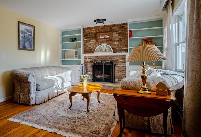 living area with built in shelves, a fireplace, baseboards, and wood finished floors