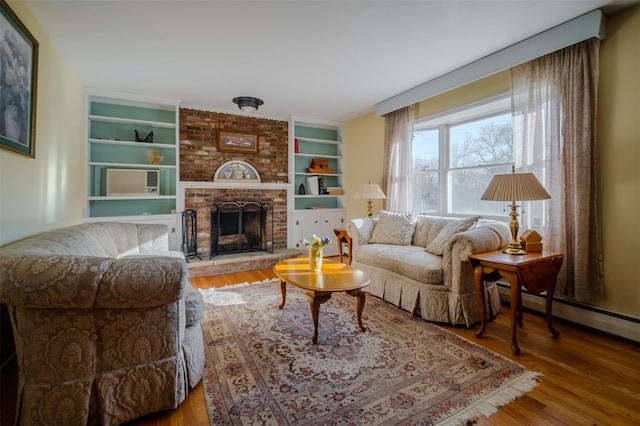 living room with built in shelves, a baseboard radiator, a fireplace, and wood finished floors