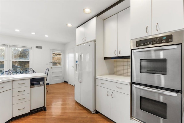 kitchen featuring decorative backsplash, white fridge with ice dispenser, stainless steel double oven, light countertops, and white cabinets