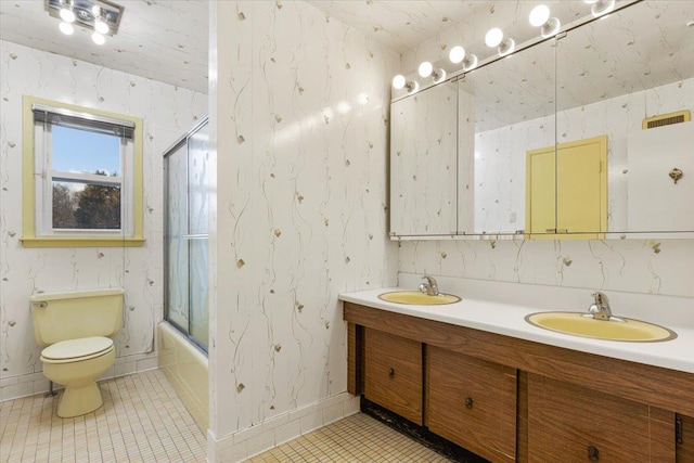 bathroom with wallpapered walls, bath / shower combo with glass door, toilet, and a sink