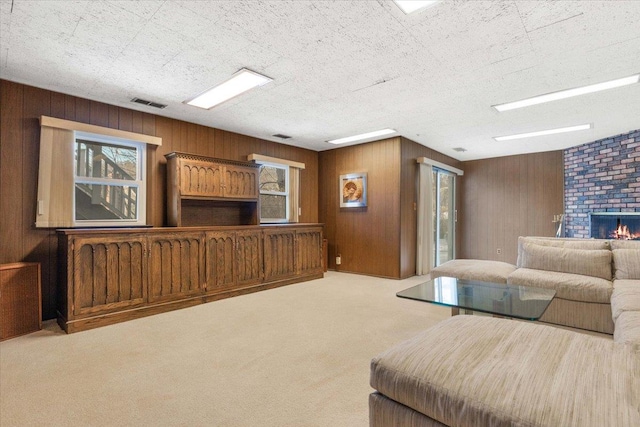 carpeted living area with visible vents, a brick fireplace, a textured ceiling, and wood walls