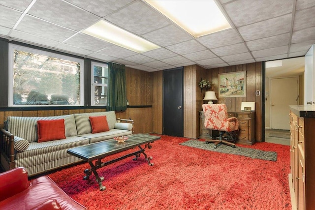 living area featuring wooden walls, carpet flooring, and a drop ceiling