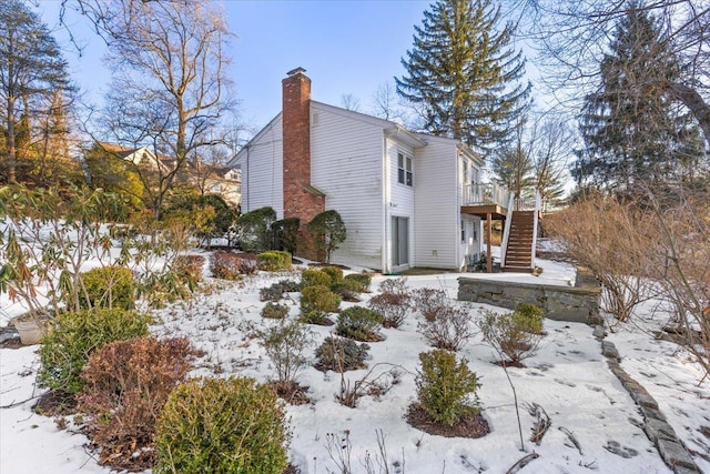 view of snow covered exterior with stairway, a wooden deck, and a chimney