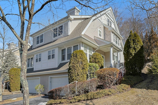 view of front of house featuring a garage, a chimney, aphalt driveway, and roof with shingles