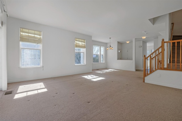 unfurnished living room with a chandelier, carpet flooring, baseboards, and stairs