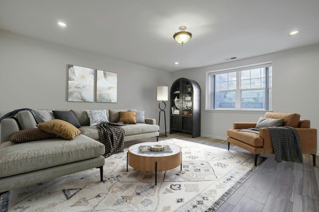 living area featuring baseboards, visible vents, arched walkways, light wood-type flooring, and recessed lighting