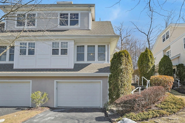 view of front facade featuring driveway, roof with shingles, an attached garage, and stucco siding