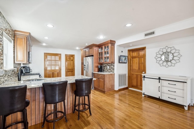 kitchen featuring a sink, visible vents, stainless steel refrigerator with ice dispenser, light stone countertops, and light wood finished floors