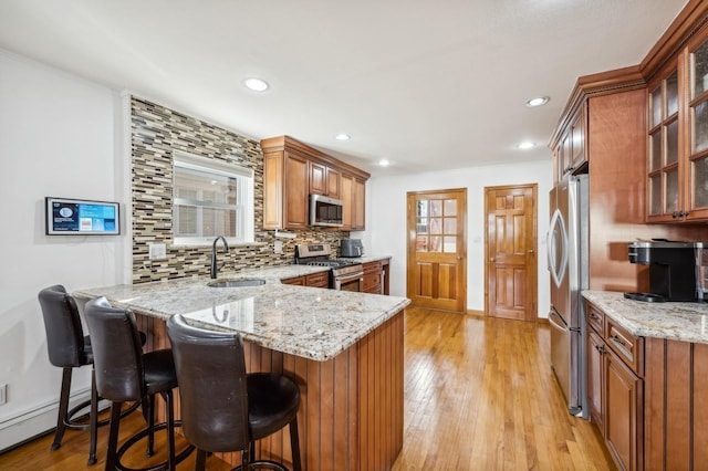 kitchen featuring brown cabinetry, decorative backsplash, a peninsula, stainless steel appliances, and a sink