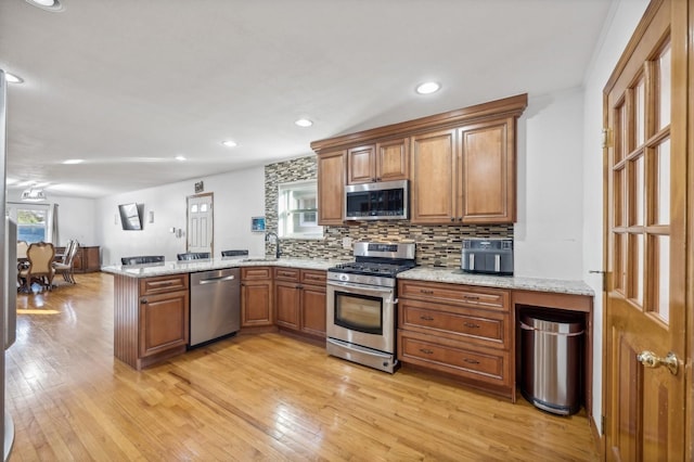 kitchen with a peninsula, light wood-style flooring, appliances with stainless steel finishes, and a sink