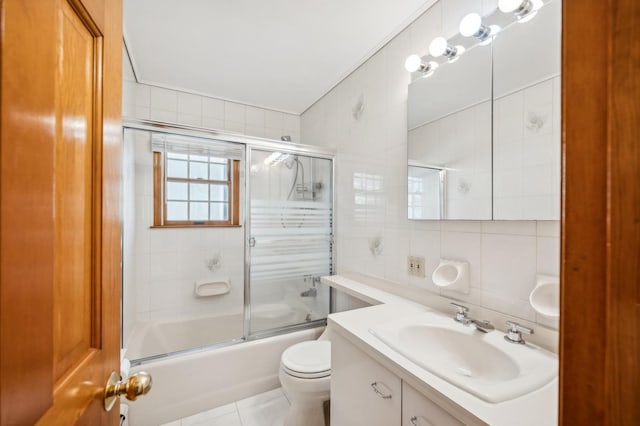 full bathroom with toilet, bath / shower combo with glass door, vanity, tile walls, and backsplash