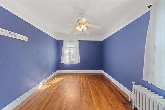 spare room featuring radiator, a ceiling fan, baseboards, and wood finished floors