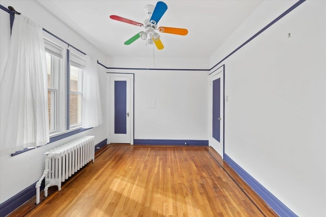 empty room featuring a ceiling fan, light wood-type flooring, radiator, and baseboards