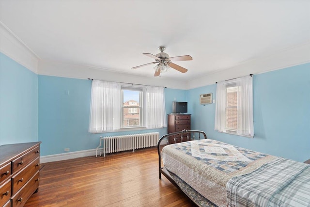 bedroom with radiator heating unit, multiple windows, and wood finished floors