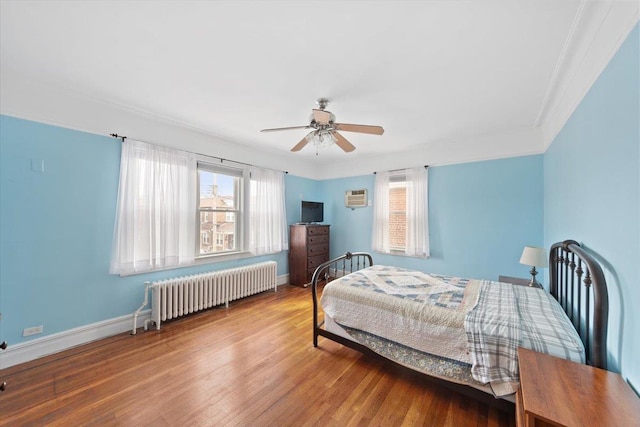 bedroom featuring baseboards, multiple windows, wood finished floors, and radiator