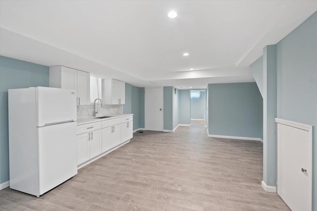 kitchen with light countertops, light wood-style flooring, freestanding refrigerator, white cabinetry, and a sink