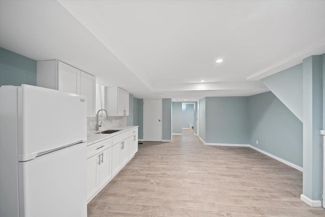 kitchen with a sink, white cabinetry, light countertops, light wood-type flooring, and freestanding refrigerator